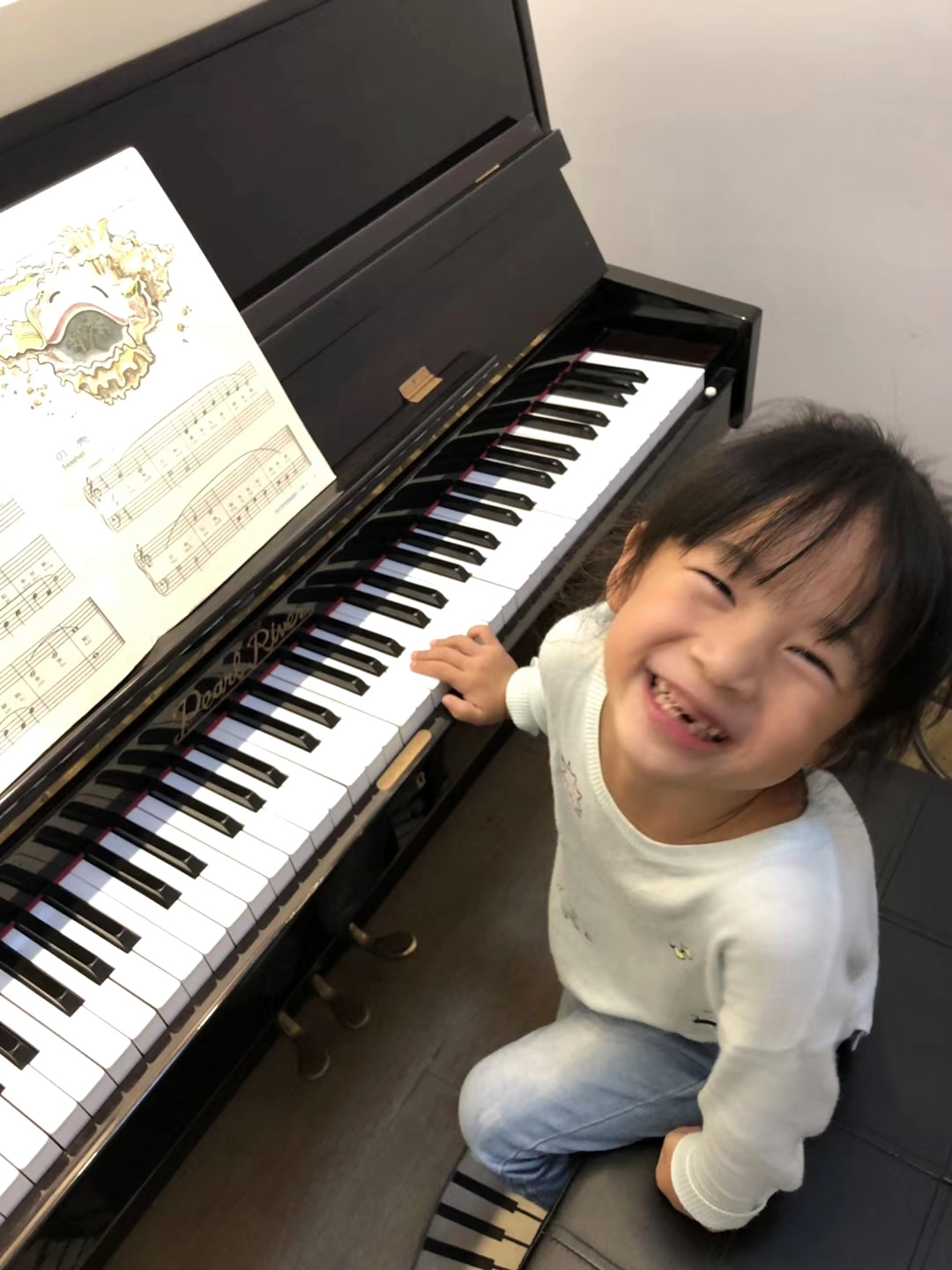 学生坐在黑色钢琴前抬头微笑,身旁保留琴键与乐谱