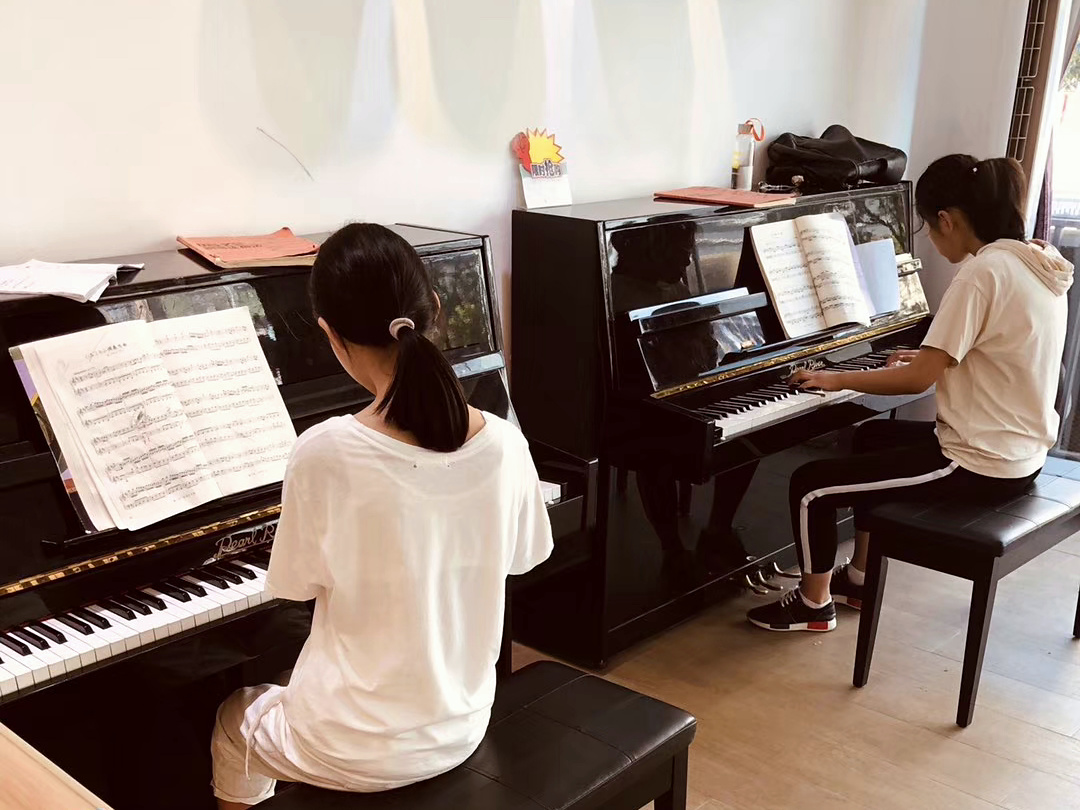 两位学生分别在两台黑色立式钢琴前练习